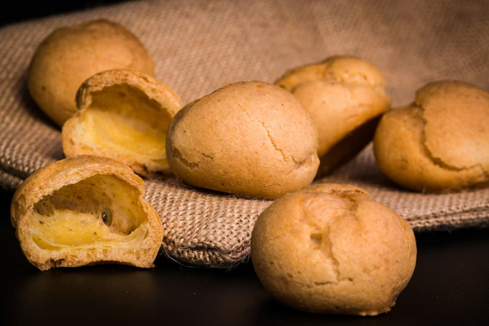 Golden Brazilian cheese bread rolls on burlap, two torn open to show the soft, chewy centre