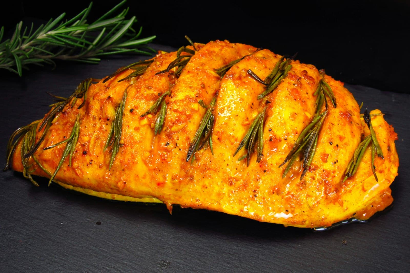 Baked chicken breast with a golden paprika crust and rosemary sprigs on a dark slate board