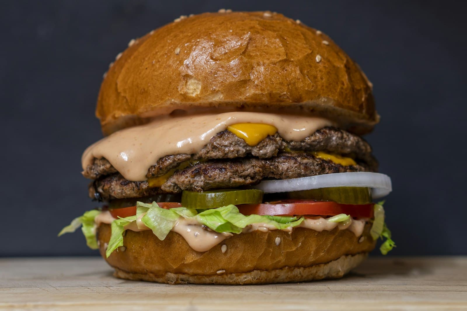 Beef burger with two grilled patties, melted cheese, pickles, onion, tomato and lettuce in a sesame bun