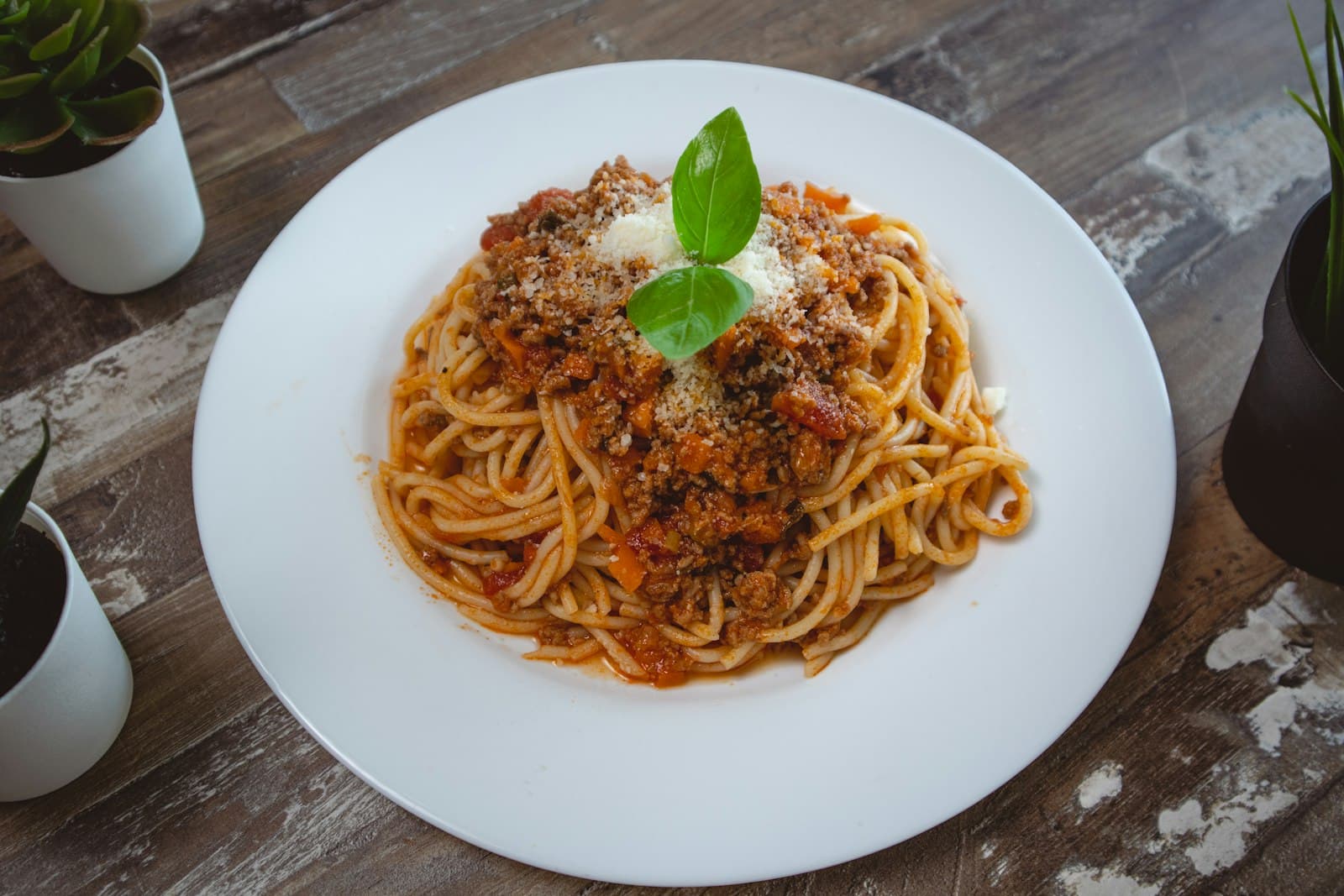 Spaghetti topped with rich meat sauce, grated parmesan and a basil leaf on a white plate