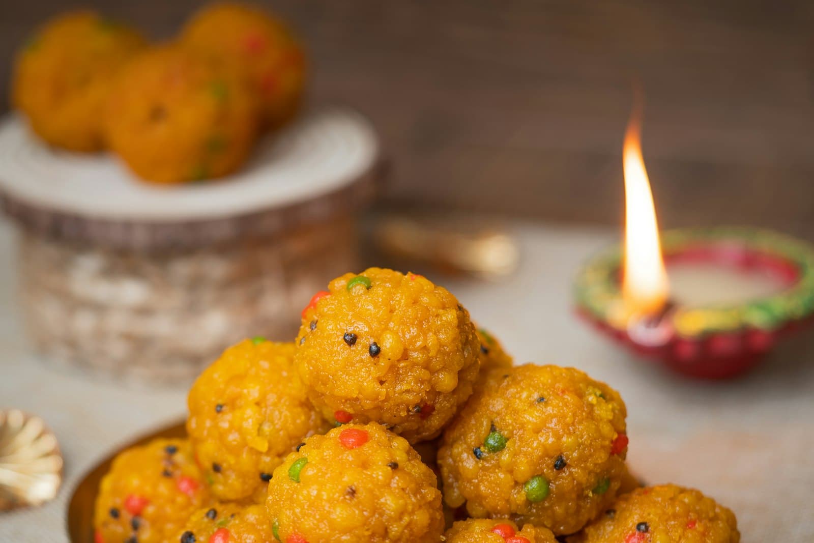 Golden boondi ladoos piled on a brass tray beside a lit clay diya and a red rose
