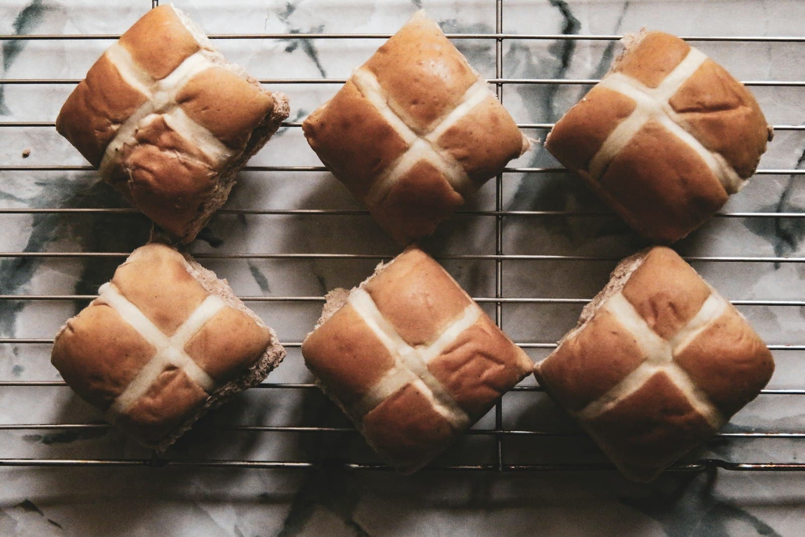 Six hot cross buns with pale piped crosses cooling on a wire rack