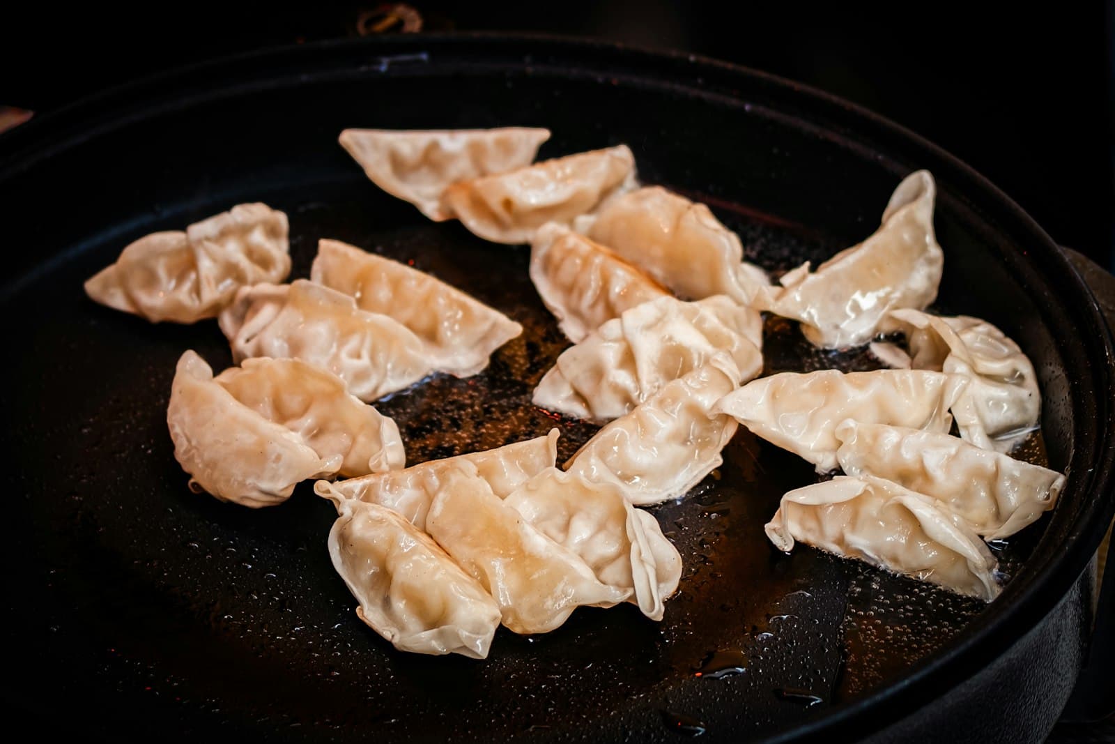 Pleated half-moon dumplings frying in a dark pan