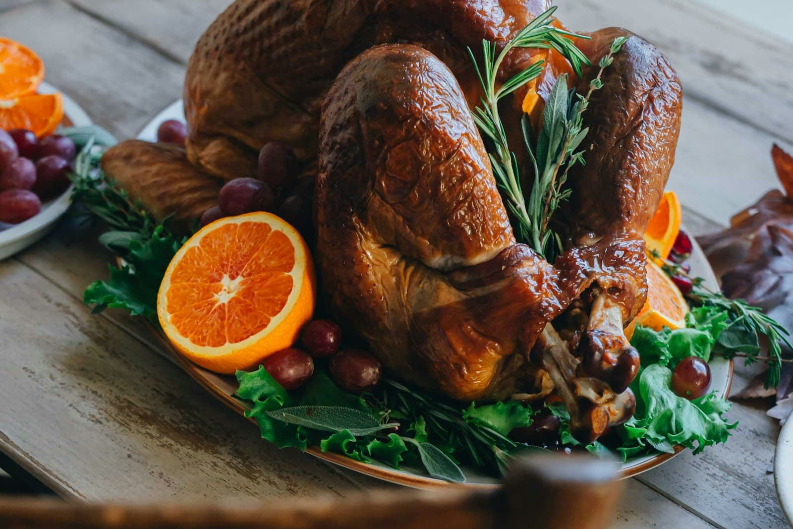 Golden roast turkey on a platter with orange halves, red grapes, rosemary and lettuce on a wooden table