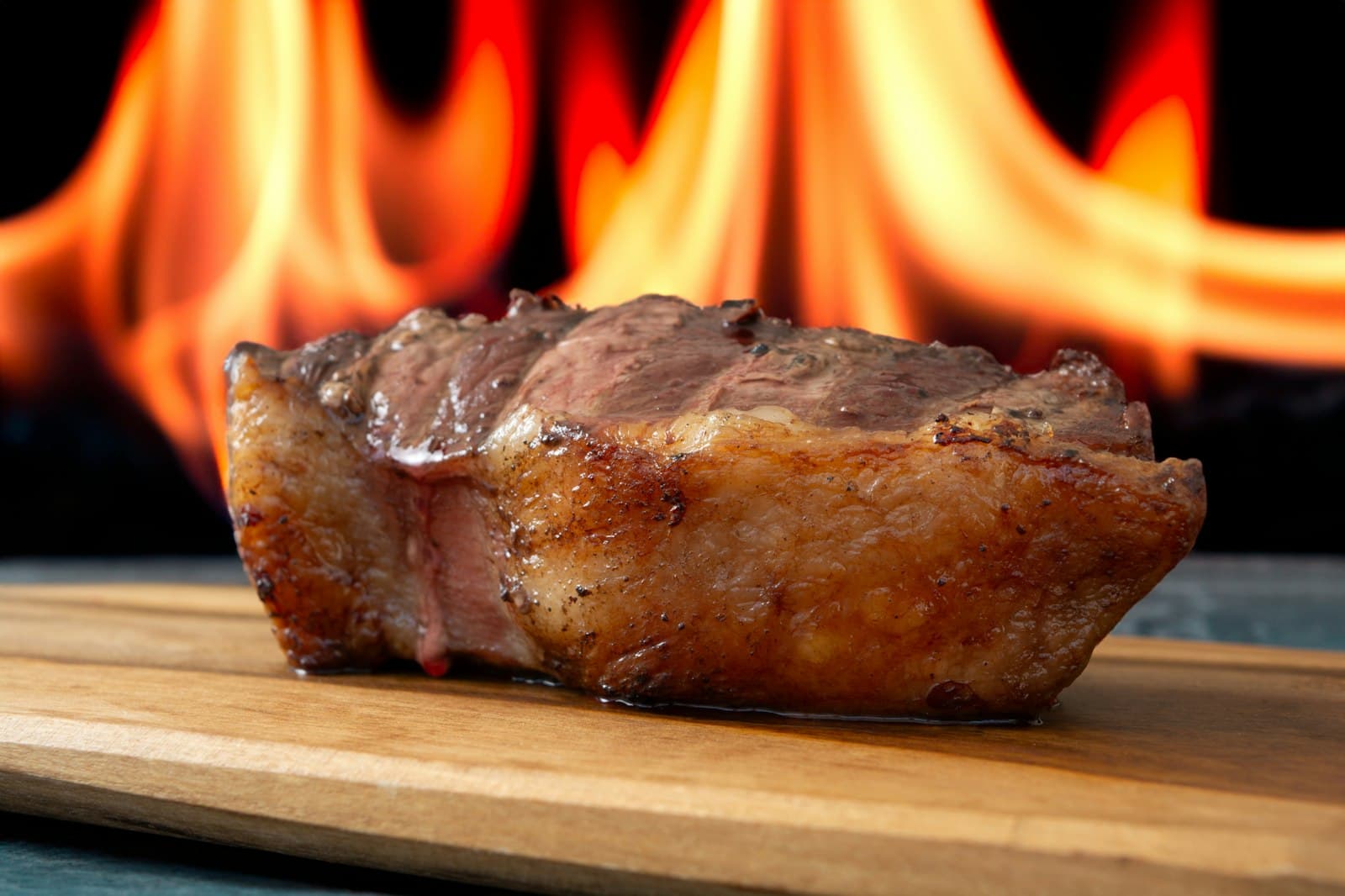 Grilled picanha steak with a golden fat cap on a wooden board in front of open flames